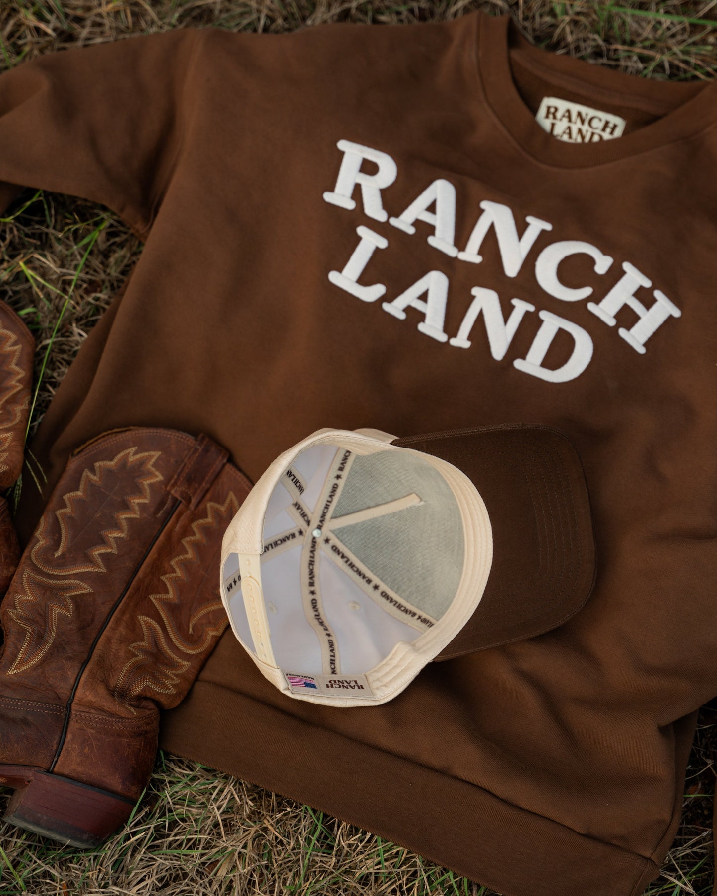 Brown 'Ranch Land' sweatshirt with cowboy boots and a cap on grass