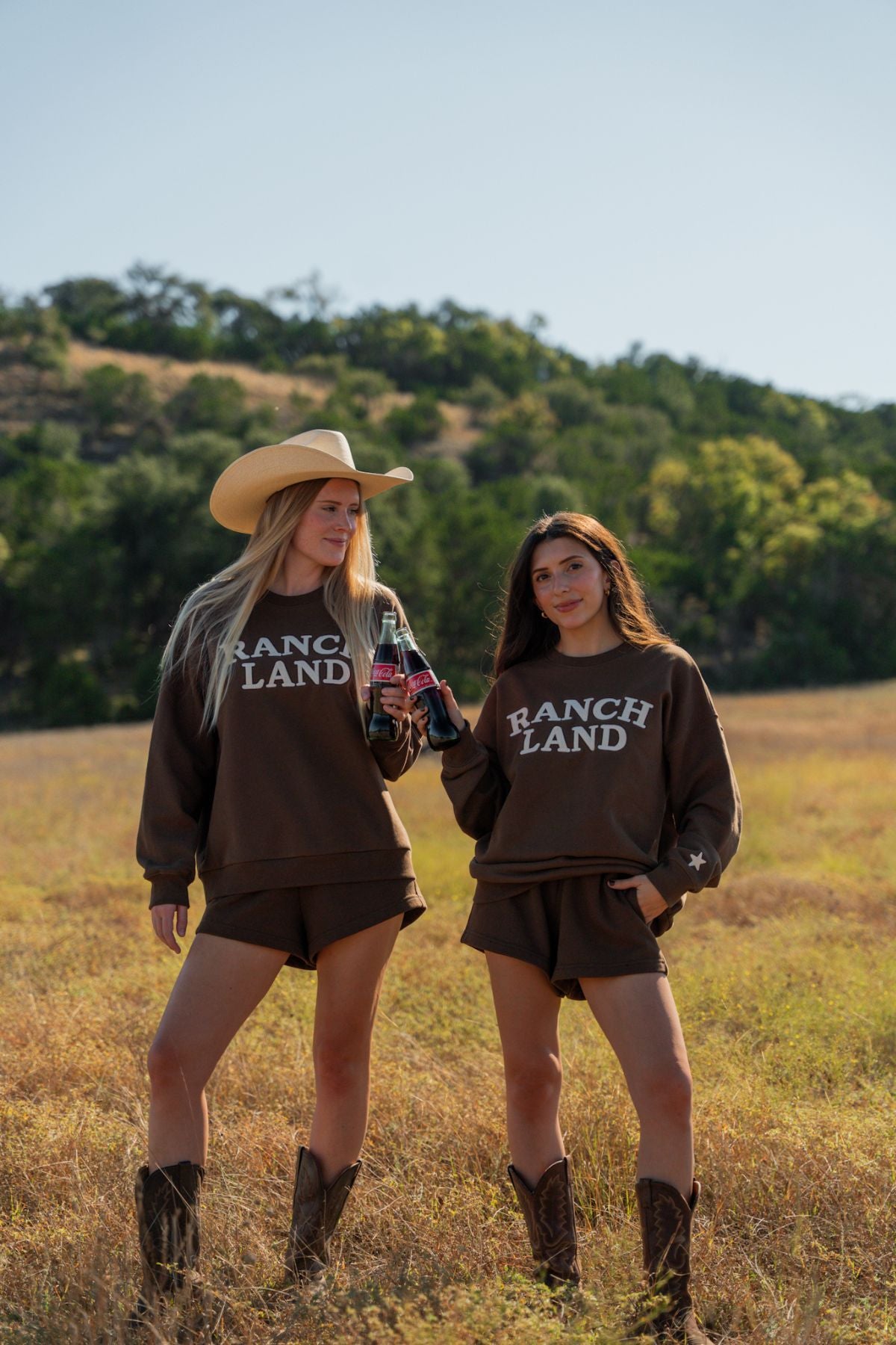 Two women in 'Ranch Land' sweatshirts standing in a field with a scenic background.