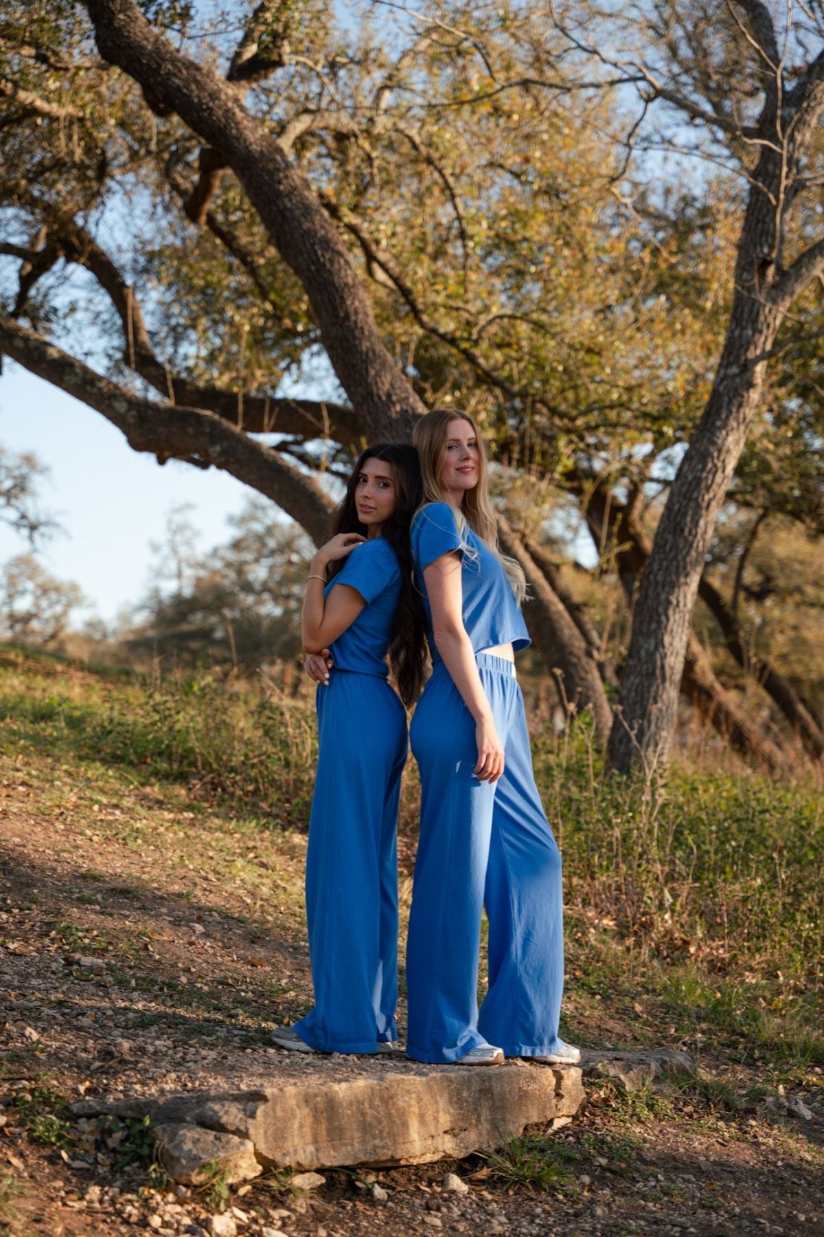 Two women in blue outfits standing on a rock with trees in the background