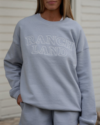Person wearing a light blue sweatshirt with 'RANCH LAND' text against a neutral background