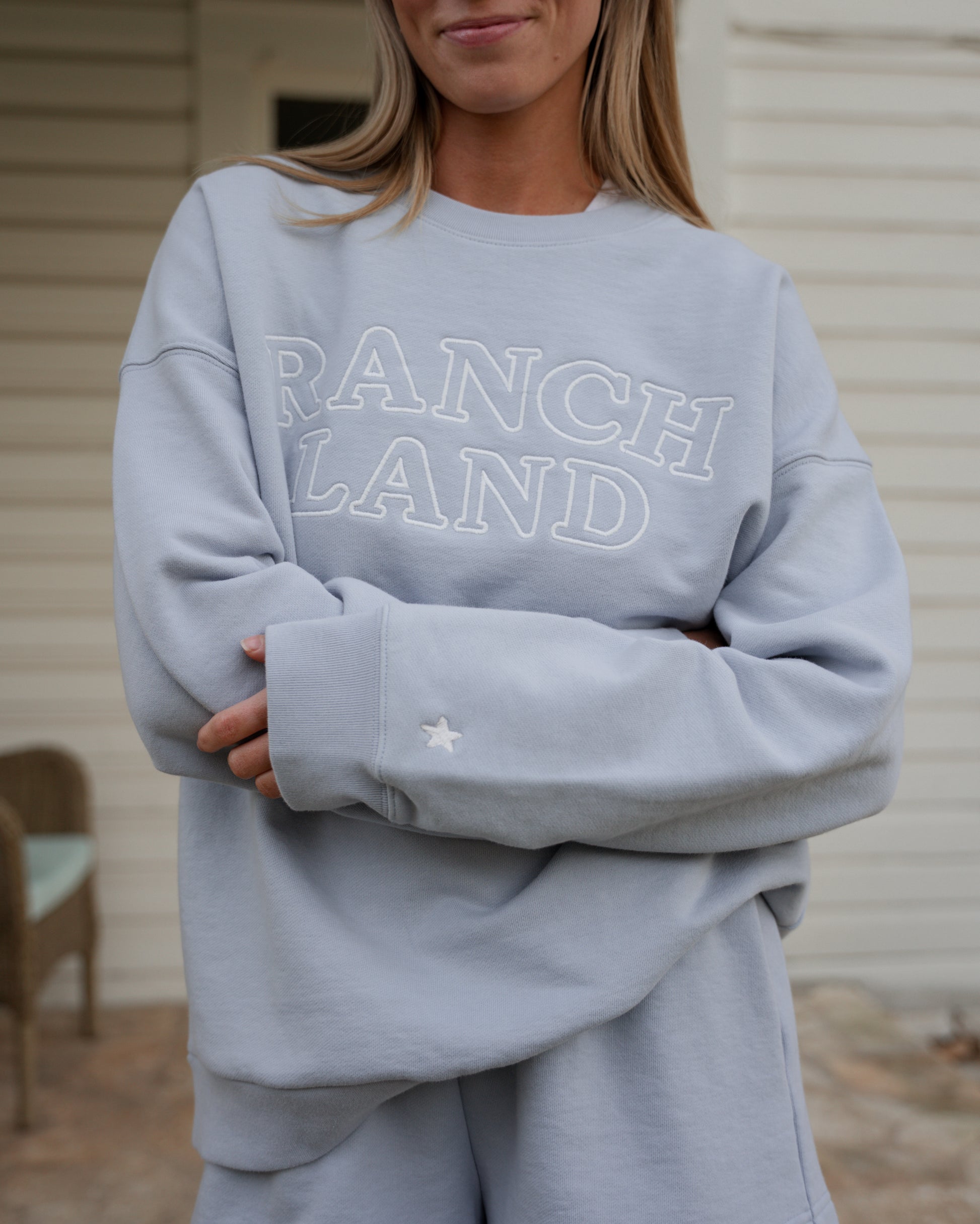 Person wearing a light blue sweatshirt with 'RANCH LAND' text, standing outdoors.