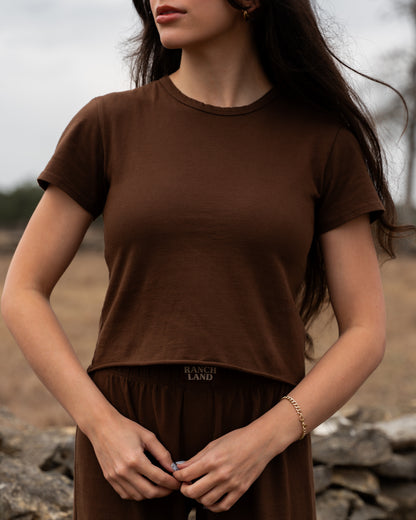 Woman wearing a brown t-shirt with 'Ranch Land' logo outdoors.