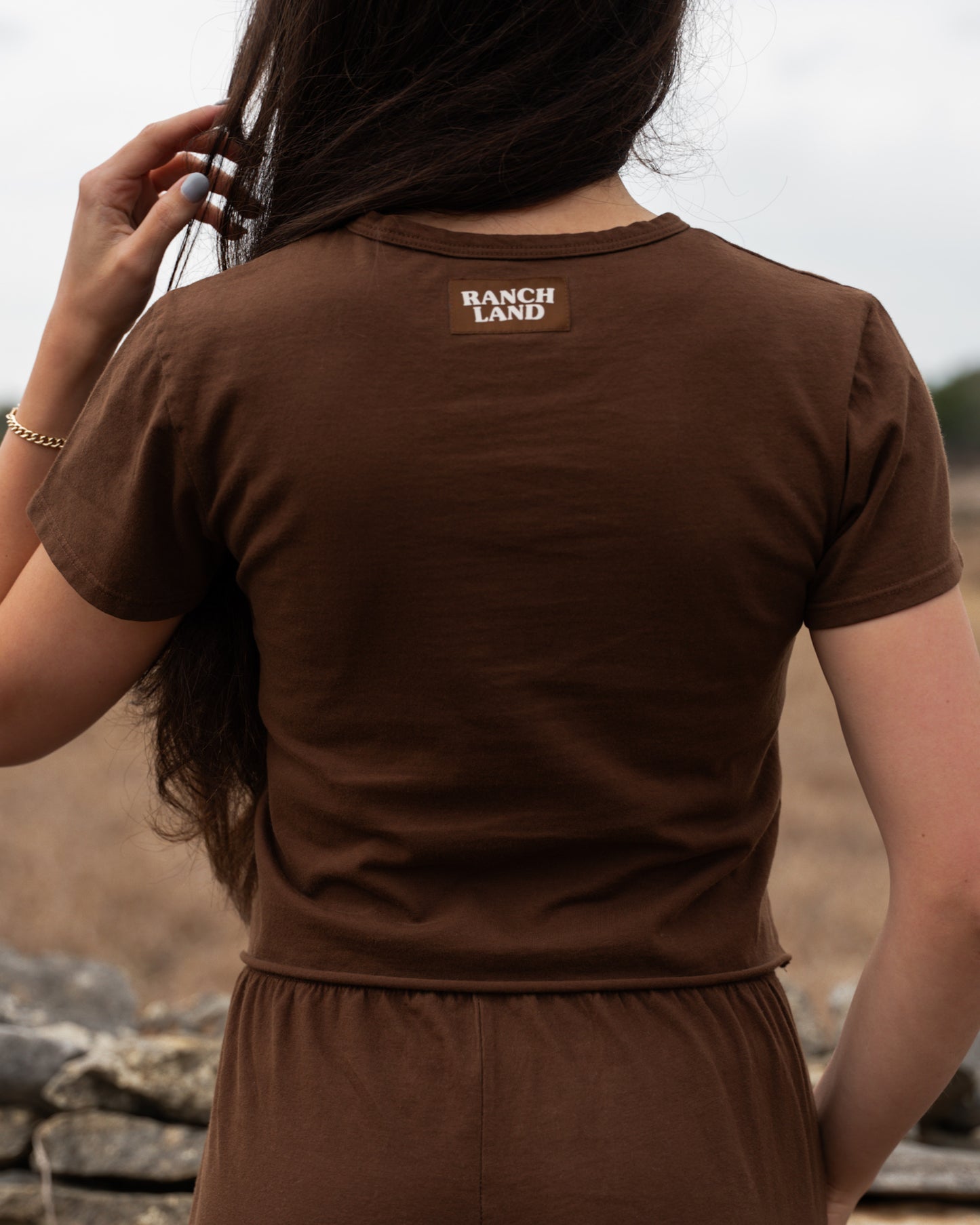 Person wearing a brown 'Ranch Land' t-shirt with a blurred natural background