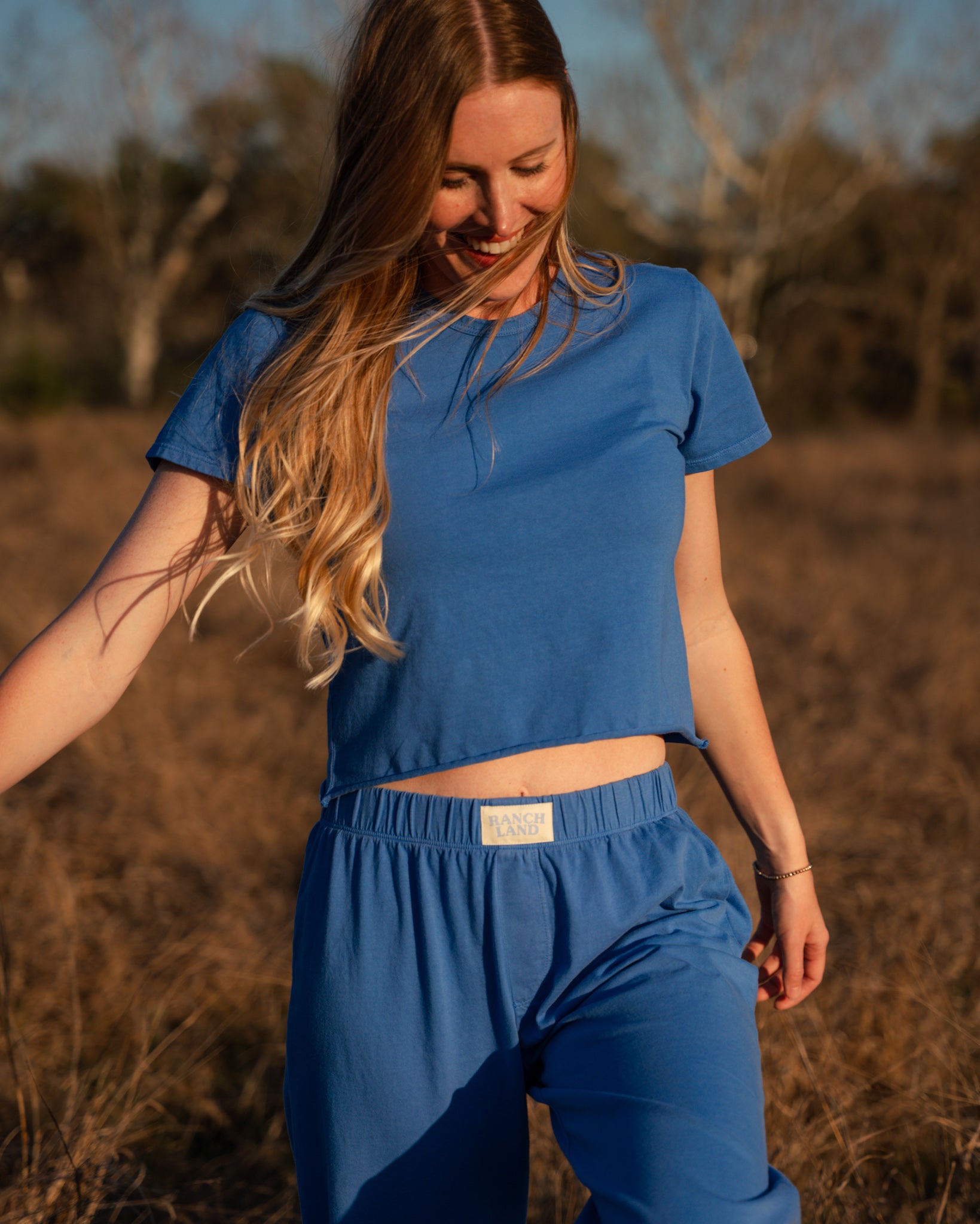 Woman wearing a blue outfit standing in a field with trees in the background