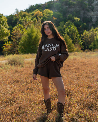 Person wearing a 'Ranch Land' sweatshirt in a field with trees in the background