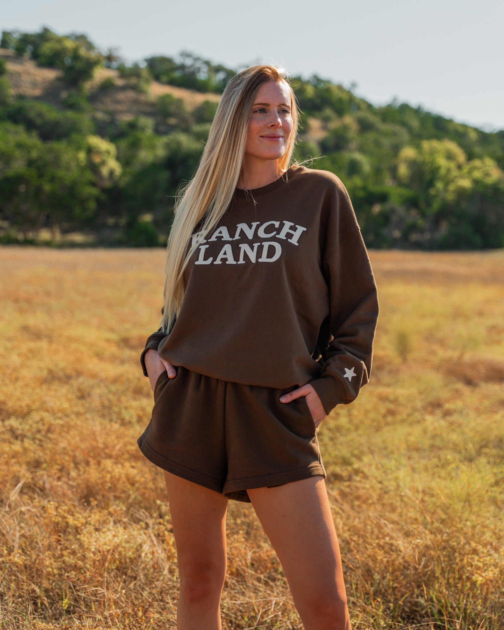 Woman wearing a 'Ranch Land' sweatshirt in a field with trees in the background