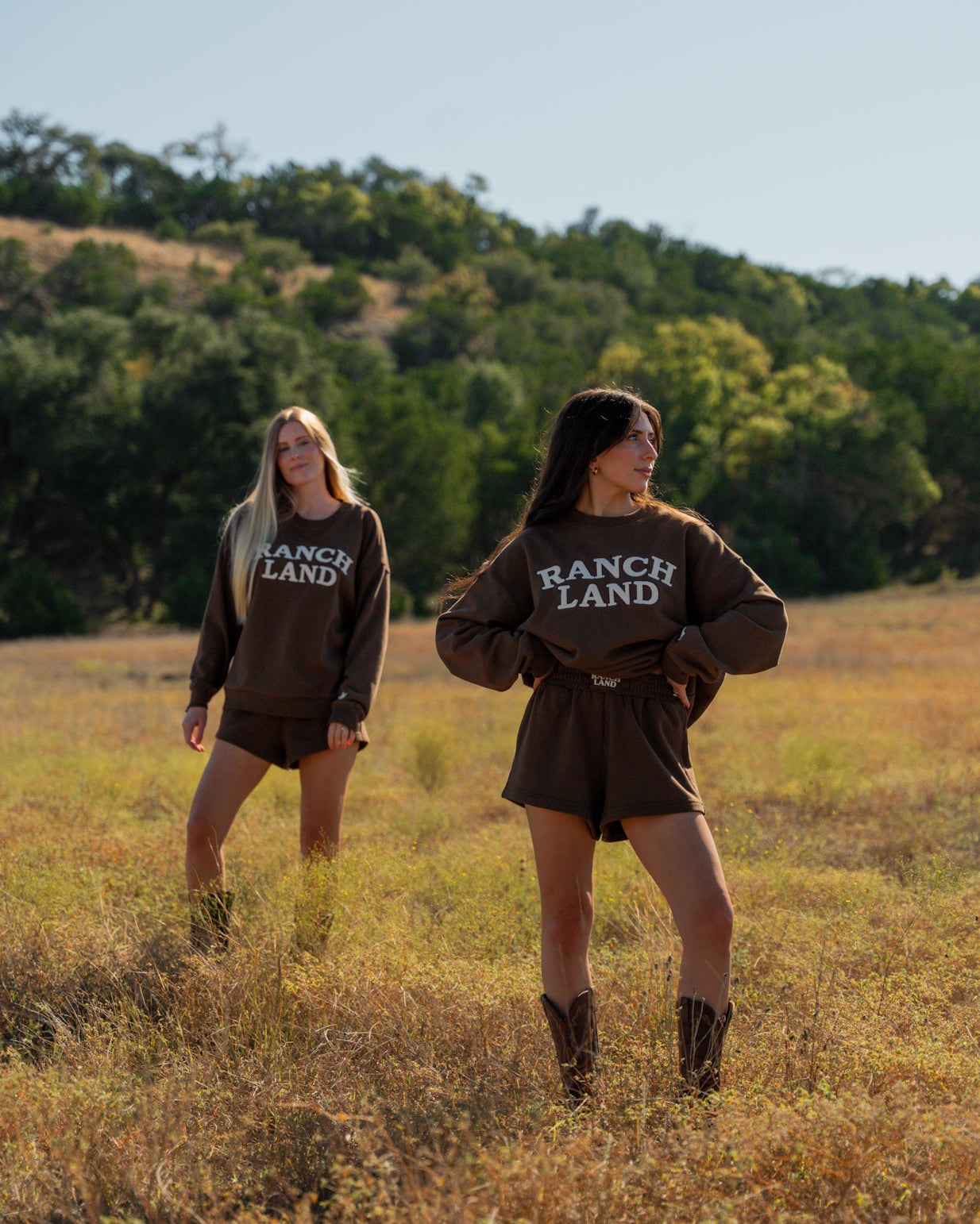 Two people wearing 'Ranch Land' sweatshirts standing in a field with trees in the background.