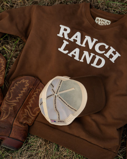 Brown 'Ranch Land' sweatshirt with cowboy boots and a cap on grass