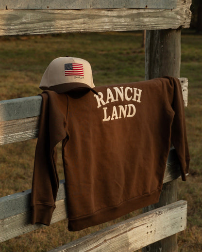 Brown 'Ranch Land' jacket and boots hanging on a wooden fence in a field.