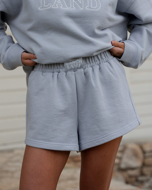 Person wearing a gray sweatshirt and shorts set with 'LAND' branding.